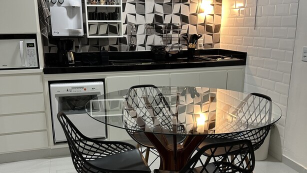Una cocina moderna con armarios blancos, encimera negra y una mesa de comedor de vidrio con sillas negras.