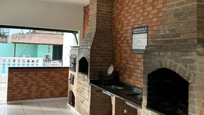 Un área de cocina al aire libre construida con ladrillos, con suelo de baldosas y un letrero que indica 'CHURCHOS DE UTILIZAÇÃO' (zona de parrilla de carbón).