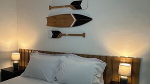 Una cama bien tendida con sábanas blancas, dos mesitas de noche con lámparas, y tres paletas de madera colgadas en la pared sobre la cama.