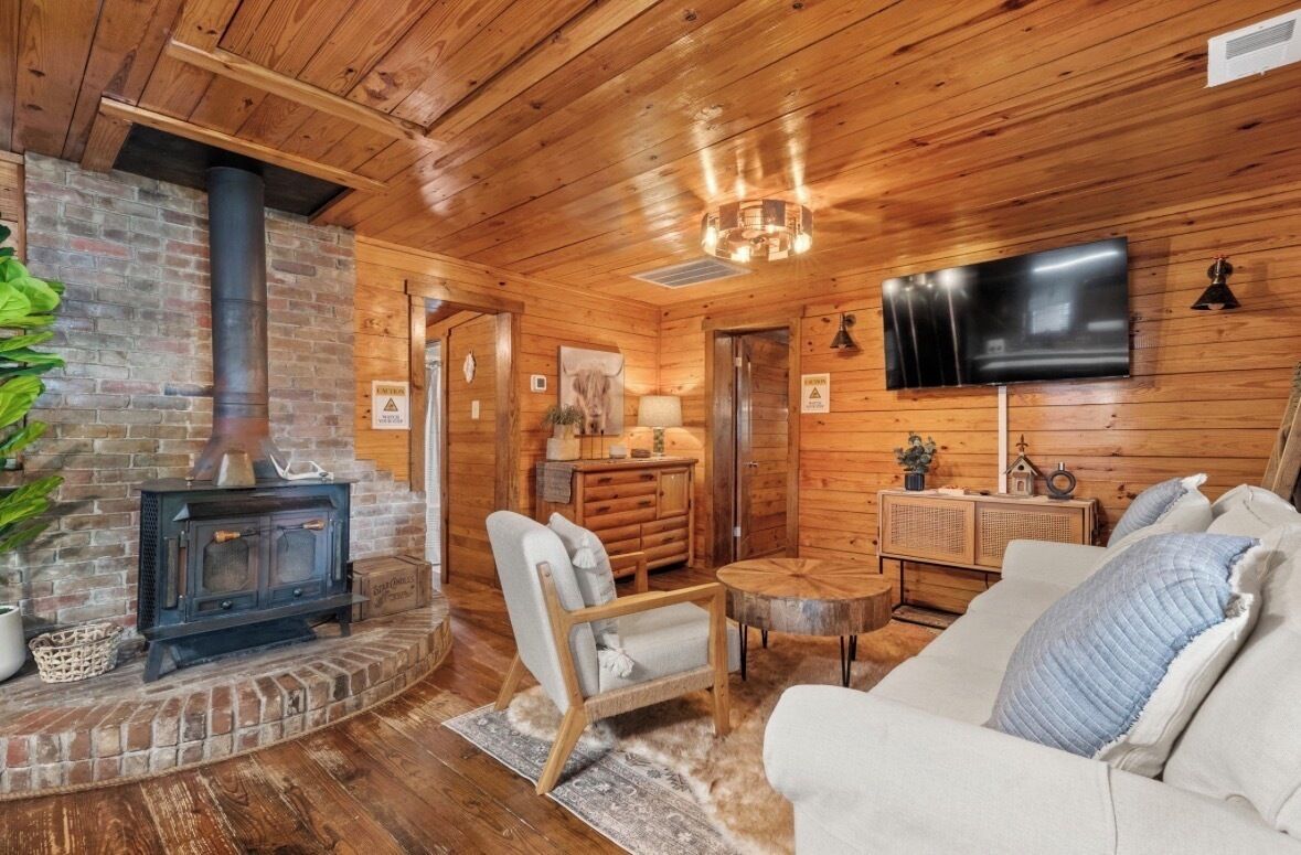 A cozy cabin interior with a fireplace, wooden walls, a flat-screen TV, and a comfortable seating area.