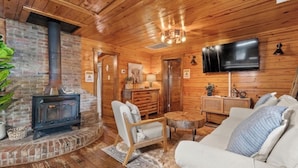 A cozy cabin interior with a fireplace, wooden walls, a flat-screen TV, and a comfortable seating area.