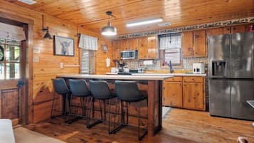 A wooden cabin interior with a kitchen area featuring a refrigerator, microwave, and bar stools.