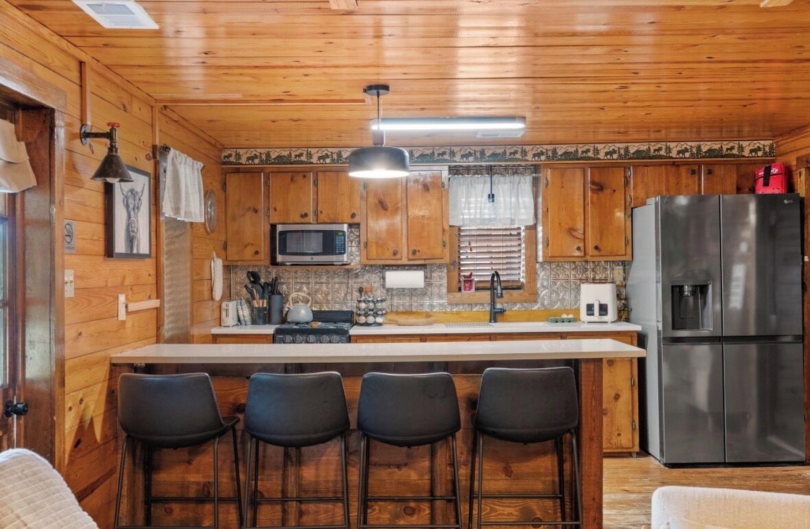 A wooden cabin interior with a kitchen area featuring a refrigerator, microwave, and bar stools.