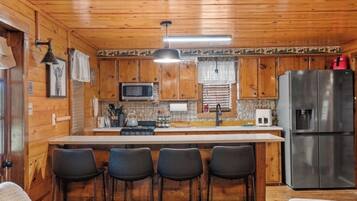 A wooden cabin interior with a kitchen area featuring a refrigerator, microwave, and bar stools.