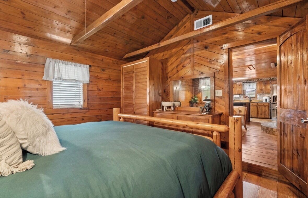 Interno di una baita di legno con un letto, una cassettiera e un angolo cottura.