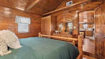 Interno di una baita di legno con un letto, una cassettiera e un angolo cottura.