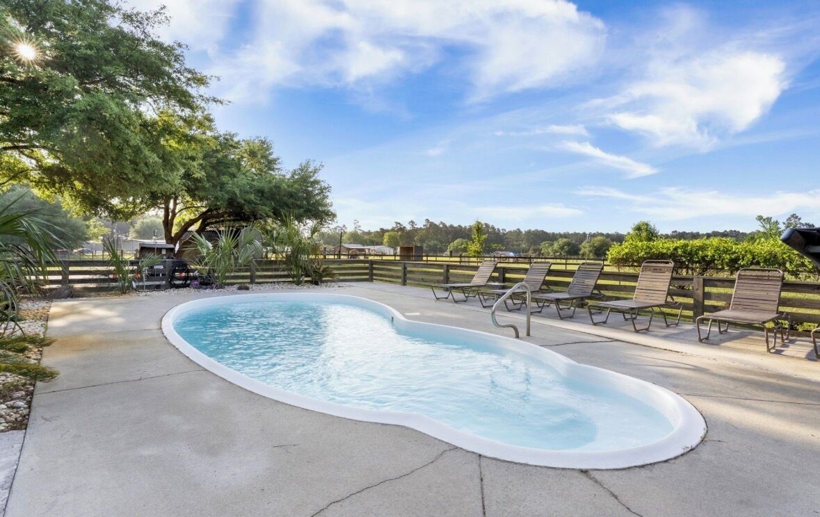 A swimming pool with a curved edge, surrounded by a wooden fence and several lounge chairs.