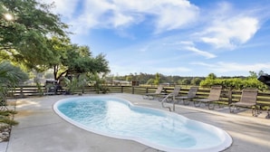 A swimming pool with a curved edge, surrounded by a wooden fence and several lounge chairs.