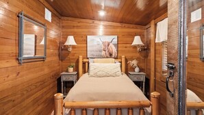 Una stanza in legno con un letto, due comodini, una lampada, uno specchio e un quadro di una mucca.