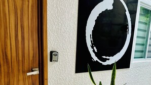 A wooden door with a number plate, a potted plant, and a large black and white abstract painting on the wall. - Espacio Libertad  (Guadalajara)