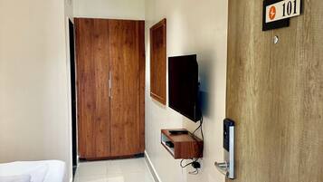 A hotel room with a bed, a wooden wardrobe, a television mounted on the wall, and a door with a number sign.