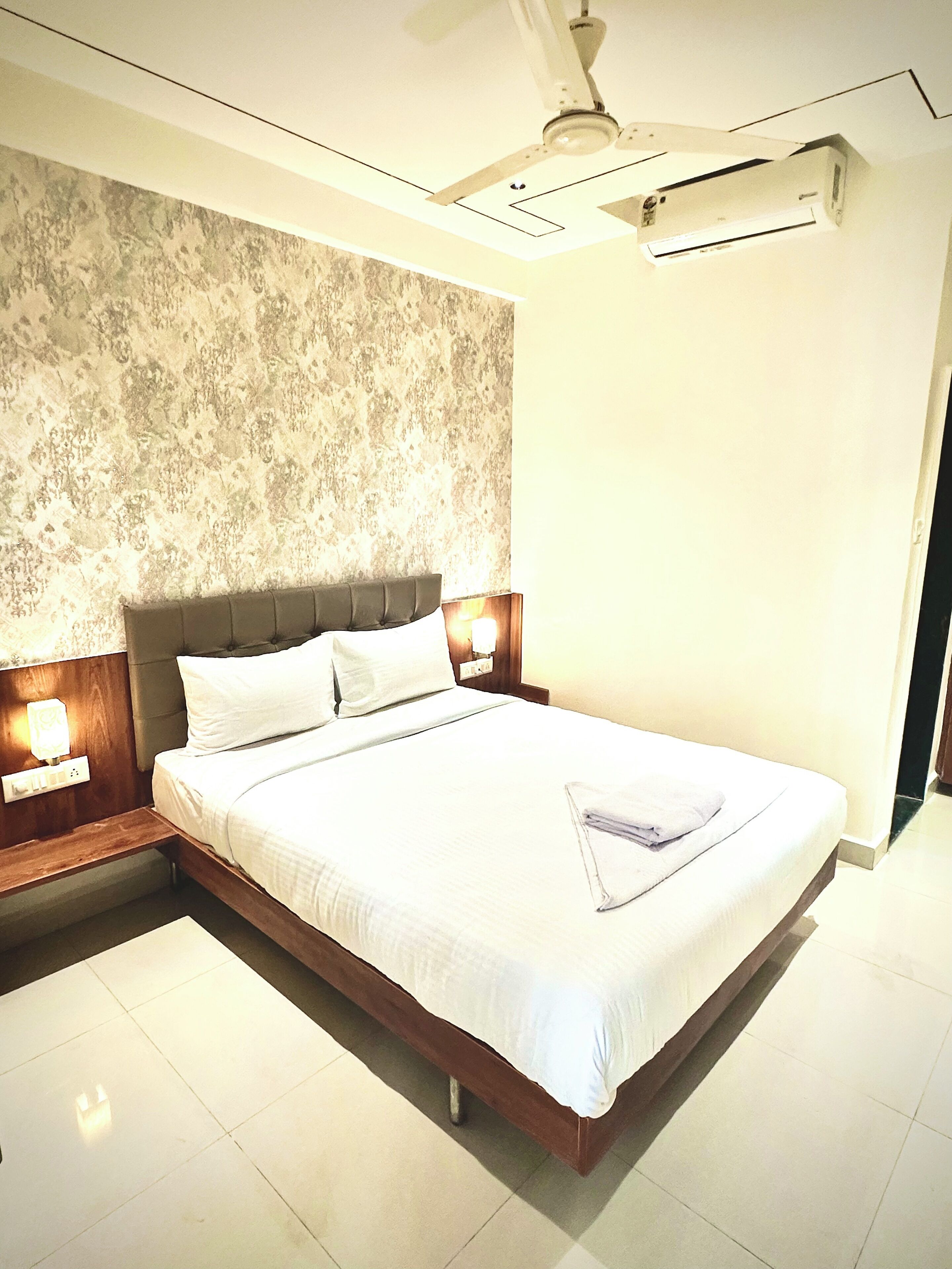Una habitación de hotel moderna con una cama grande, un muro con textura, un ventilador de techo y un equipo de aire acondicionado.