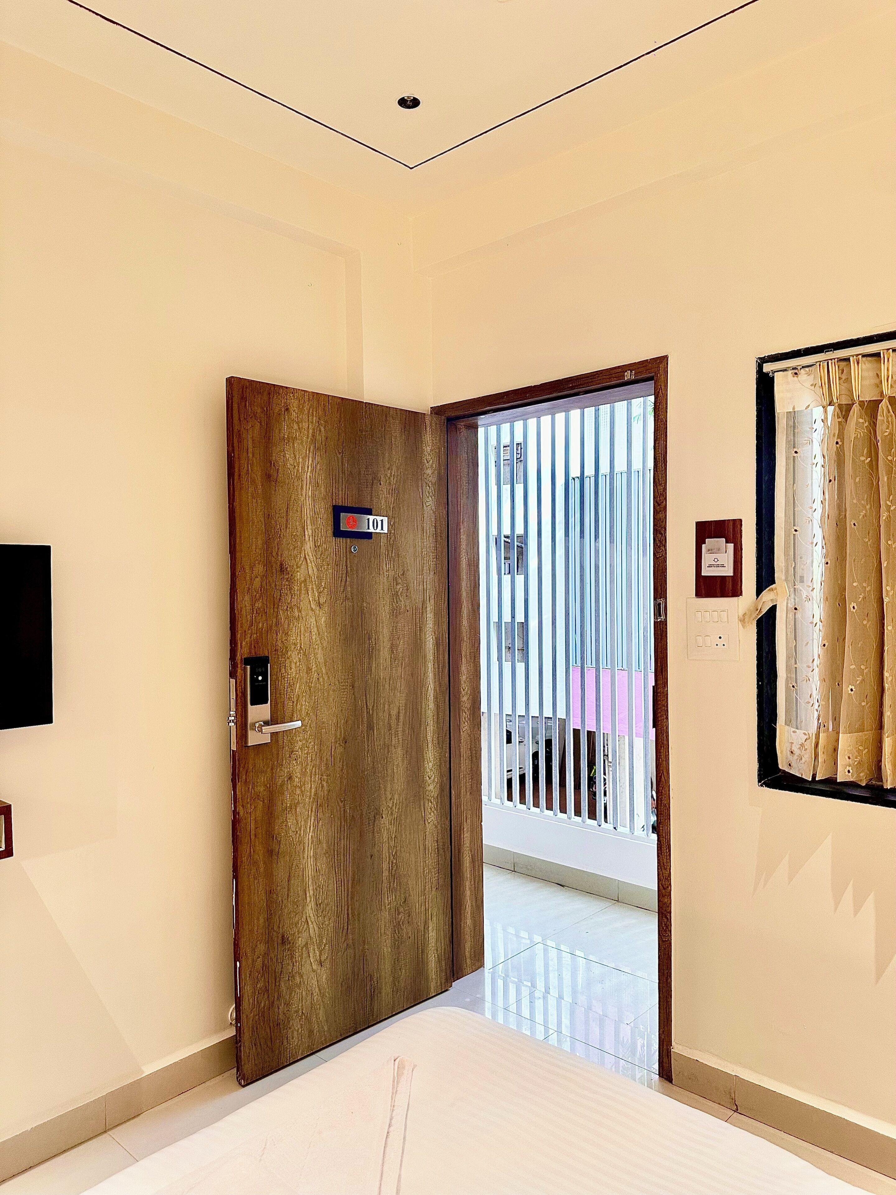 A hallway with a wooden door marked with the number 101, a security keypad, and a view through a barred window.