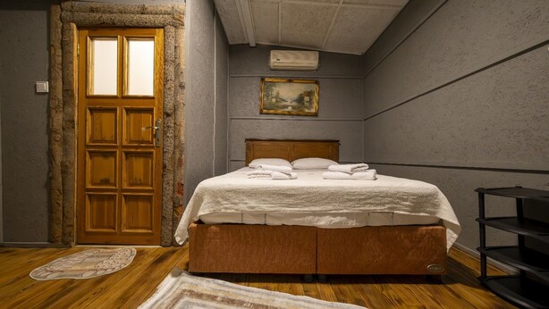 A bedroom with a wooden bed, a large window, a painting on the wall, and a wooden door. - İda Tahtalıköy Bungalov (Edremit)