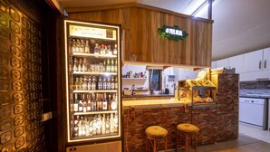 A bar area with a refrigerated display of alcoholic beverages, a wooden counter, and two stools. - İda Tahtalıköy Bungalov (Edremit)