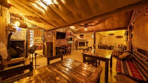 A cozy, rustic interior with a wooden ceiling, a fireplace, and a dining area with wooden tables and chairs. - İda Tahtalıköy Bungalov (Edremit)