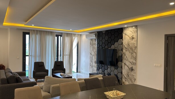 A modern living room with a sofa, chairs, a dining table, and a TV mounted on a hexagonal wall. - Luxury apartment with lake view in Dakar (Dakar)