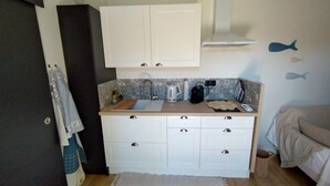 A compact kitchen with white cabinets, a sink, and a countertop. There are fish decals on the wall, a kettle, and a coffee maker.