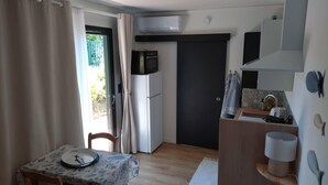 A compact kitchen with a refrigerator, microwave, and a small sink. There's a dining area with a table and chairs, and a door leading to a balcony.