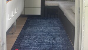 A compact RV interior with a kitchenette, a small seating area, and a window providing a view of greenery. - You know you want to do it! Glamping. Charming Airstream in Enchanting Ashtabula (Ashtabula)