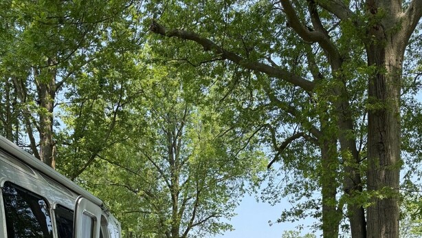 A white RV parked on a wooden deck with outdoor seating and a view of a house and water in the background. - You know you want to do it! Glamping. Charming Airstream in Enchanting Ashtabula (Ashtabula)