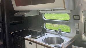 A compact kitchenette with a stove, sink, and storage cabinets. - You know you want to do it! Glamping. Charming Airstream in Enchanting Ashtabula (Ashtabula)
