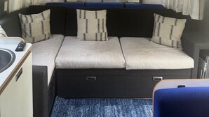 A compact RV interior with a kitchenette, a dining area, and a sleeping berth with a view of the outdoors. - You know you want to do it! Glamping. Charming Airstream in Enchanting Ashtabula (Ashtabula)