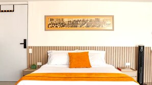Une chambre d’hôtel avec un lit, une table de chevet, une lampe de chevet, un radiateur et un tableau encadré au mur.