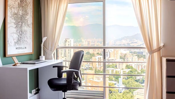 Une pièce comprenant un bureau, une chaise et une grande fenêtre avec des rideaux.
