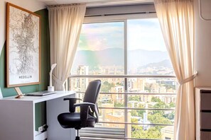A room with a desk, chair, and a large window with curtains.