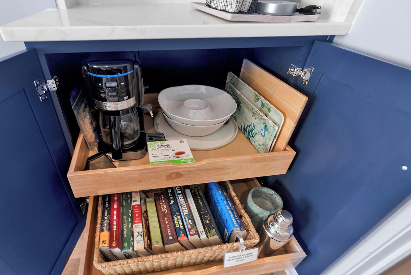 Ein kleiner Küchenbereich mit Kaffeemaschine, Teebeutel, einer Schüssel und einem Tablett mit Buch und Tasse.