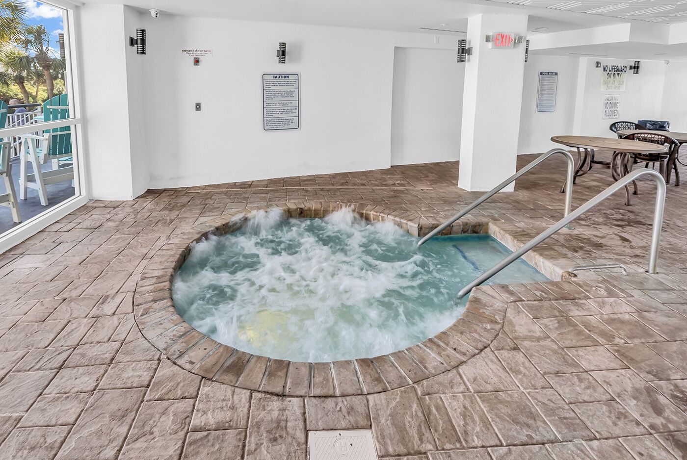 Un jacuzzi con una escalera metálica, rodeado de suelo de piedra y vistas al exterior a través de un ventanal.