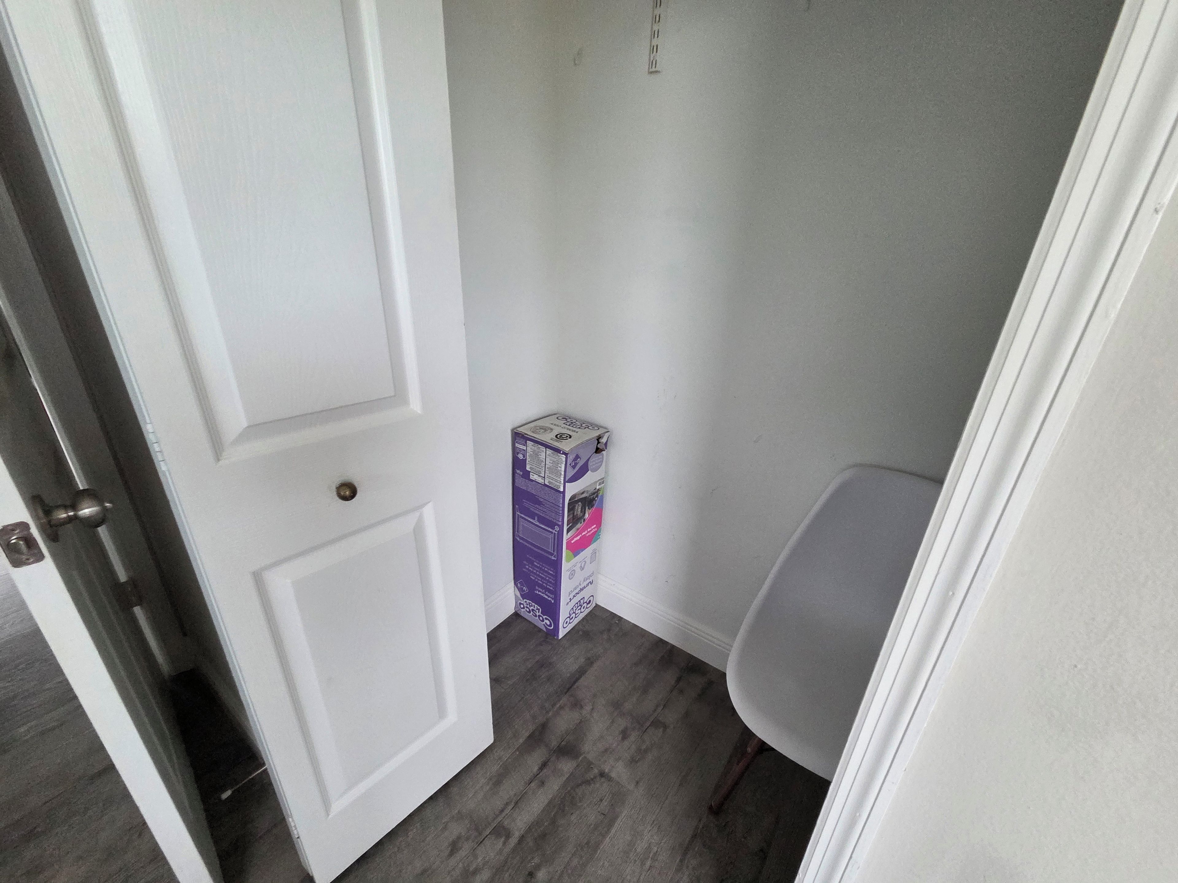 Een kamer met een witte deur, een grijze stoel en een doos op de vloer.