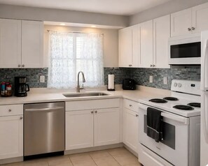 A modern kitchen with white cabinets, a stainless steel dishwasher, a built-in oven, and a microwave.
