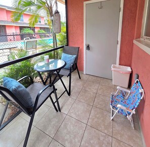 Ein Balkon mit Tisch, zwei Stühlen, einer Mülltonne und einer Tür.