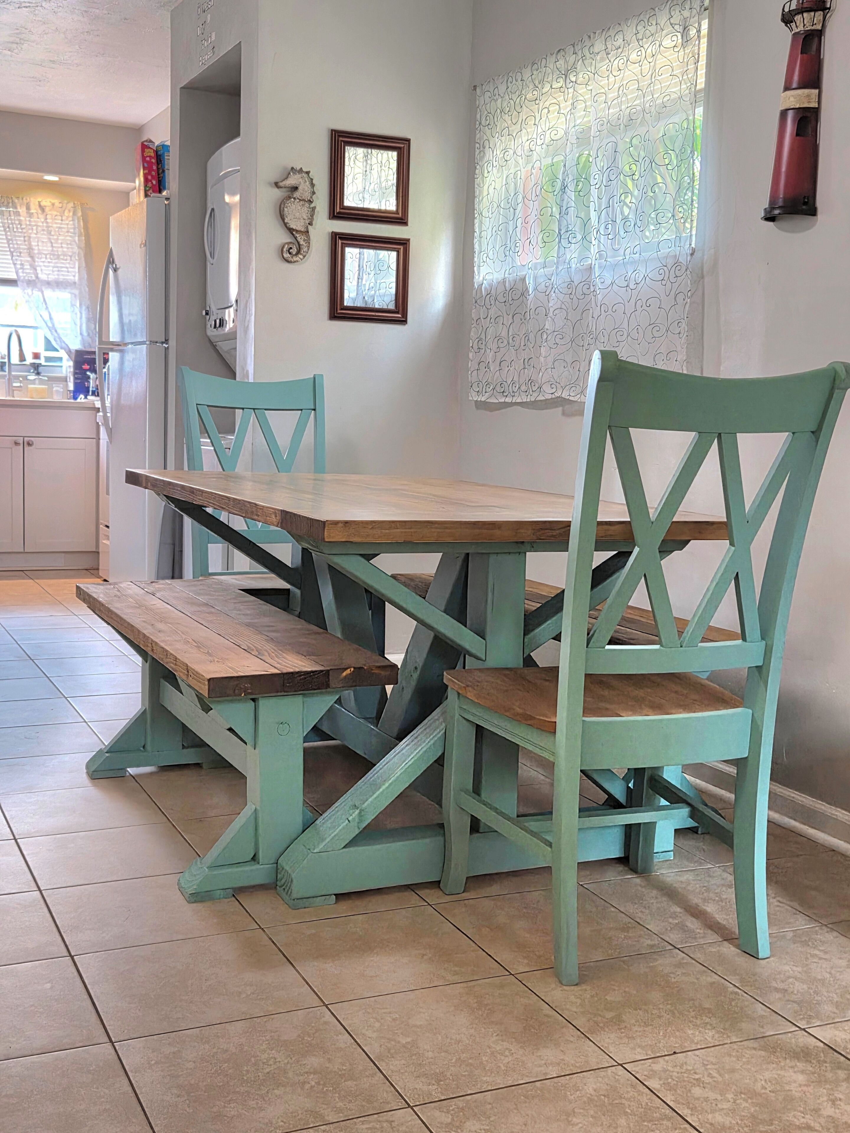A dining area with a wooden table and teal chairs, a refrigerator, and a wall-mounted light fixture.