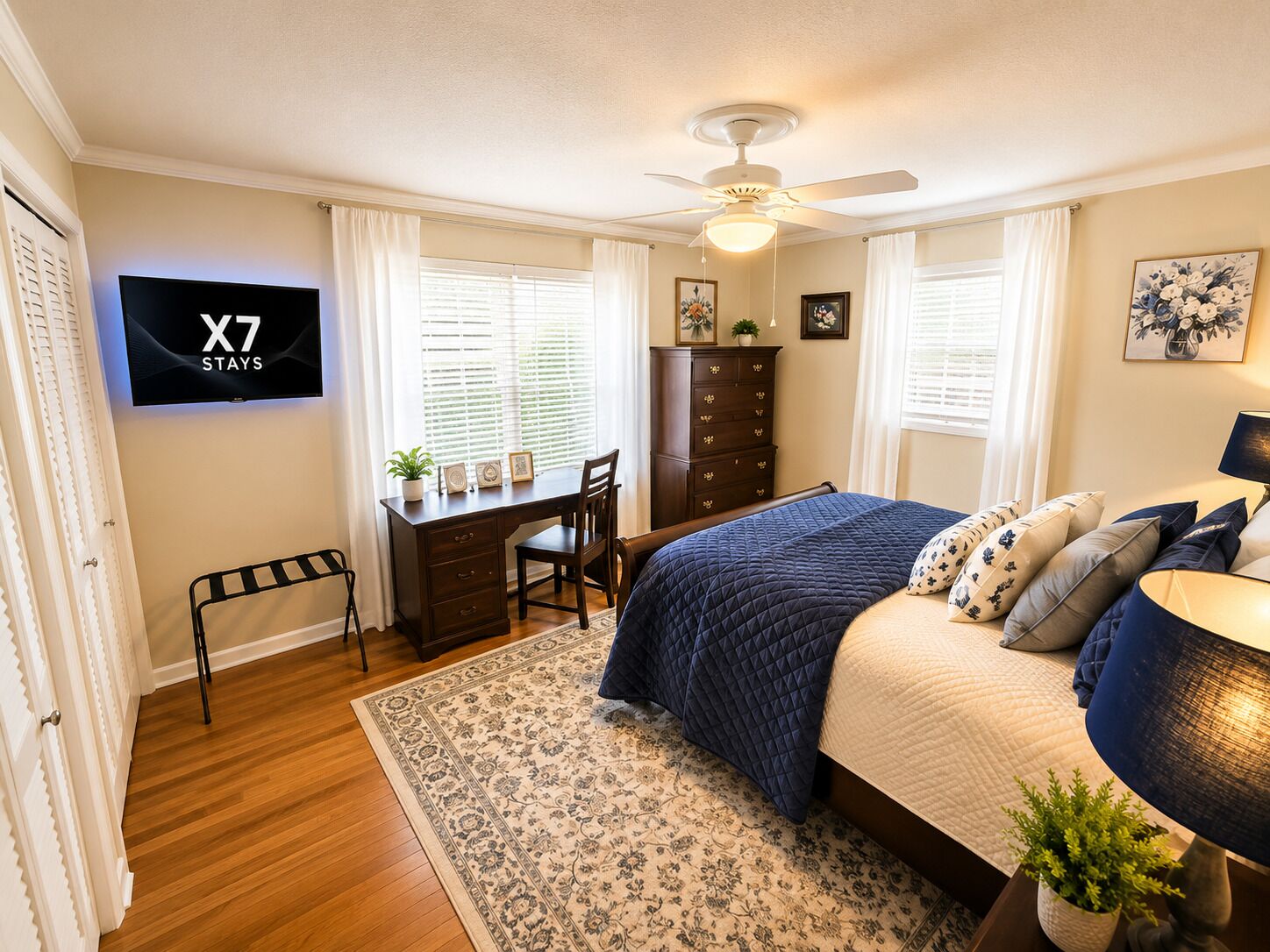 Une chambre à coucher comprenant un lit, un bureau, une chaise, une armoire et un téléviseur affichant le message « X7 STAYS ».
