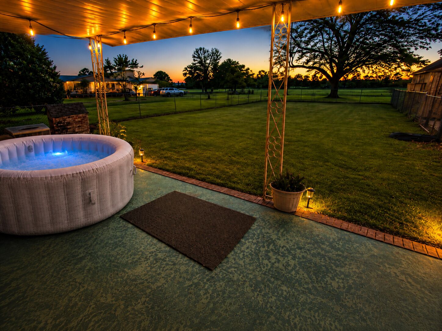 Un espace extérieur avec un jacuzzi, une terrasse couverte, des guirlandes lumineuses et une pelouse.