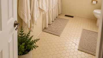 A bathroom with a hexagonal tile floor, a shower with a gold curtain, a toilet, and a window with blinds.