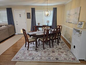 A dining area with a wooden table, chairs, and a floral rug. There is a chandelier above the table and a painting on the wall. - Hot Tub + Fenced Yard | Family & Pet Friendly (Dothan)
