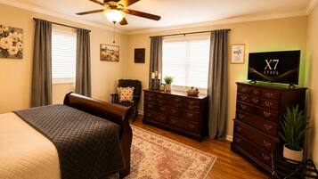 Une chambre à coucher comprenant un lit, une commode, un téléviseur et un ventilateur de plafond.