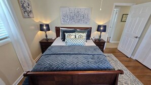 Un dormitorio con una cama de madera, dos mesitas de noche con lámparas, una gran obra de arte floral sobre la cama y una puerta a la derecha.