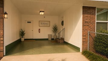Une entrée abritée, agrémentée d’une pancarte « Bienvenue », d’un extincteur et d’un escalier menant au bâtiment principal.