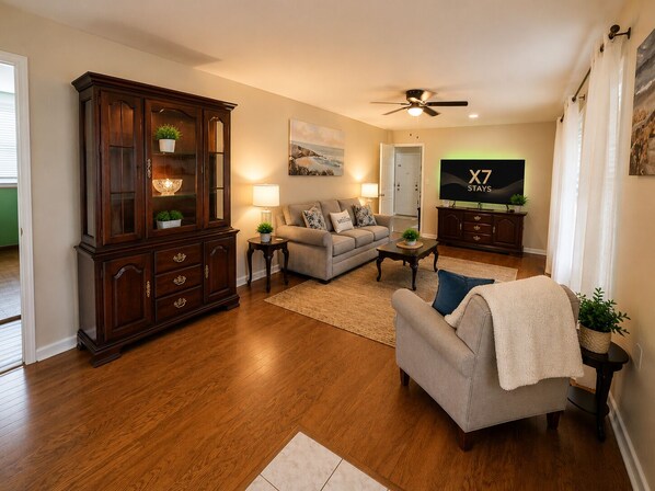 A living room with a dark wood cabinet, a grey sofa, a television, and a ceiling fan.