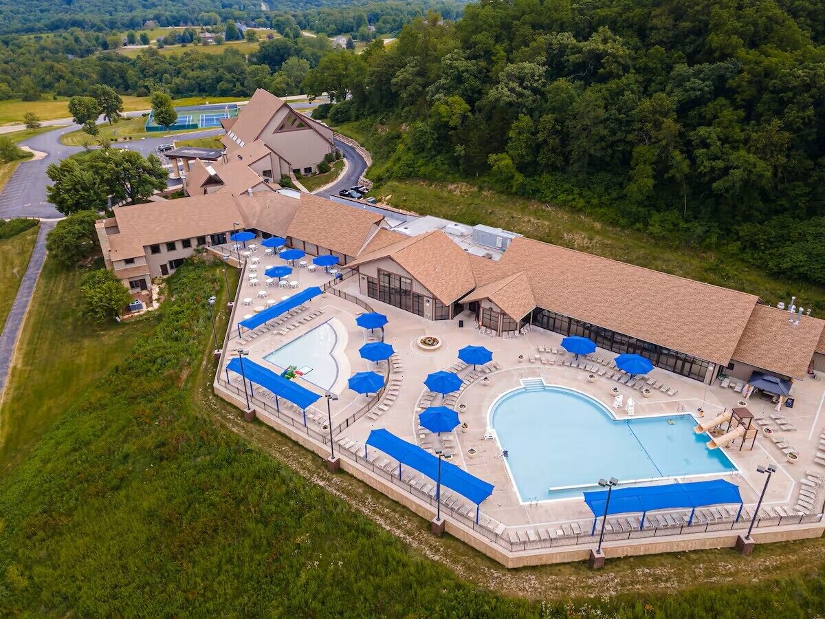 An aerial view of a resort with a large swimming pool, sun loungers, and umbrellas.