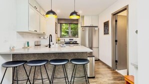 Una cocina moderna con una isla central, taburetes de bar, electrodomésticos de acero inoxidable e iluminación colgante.