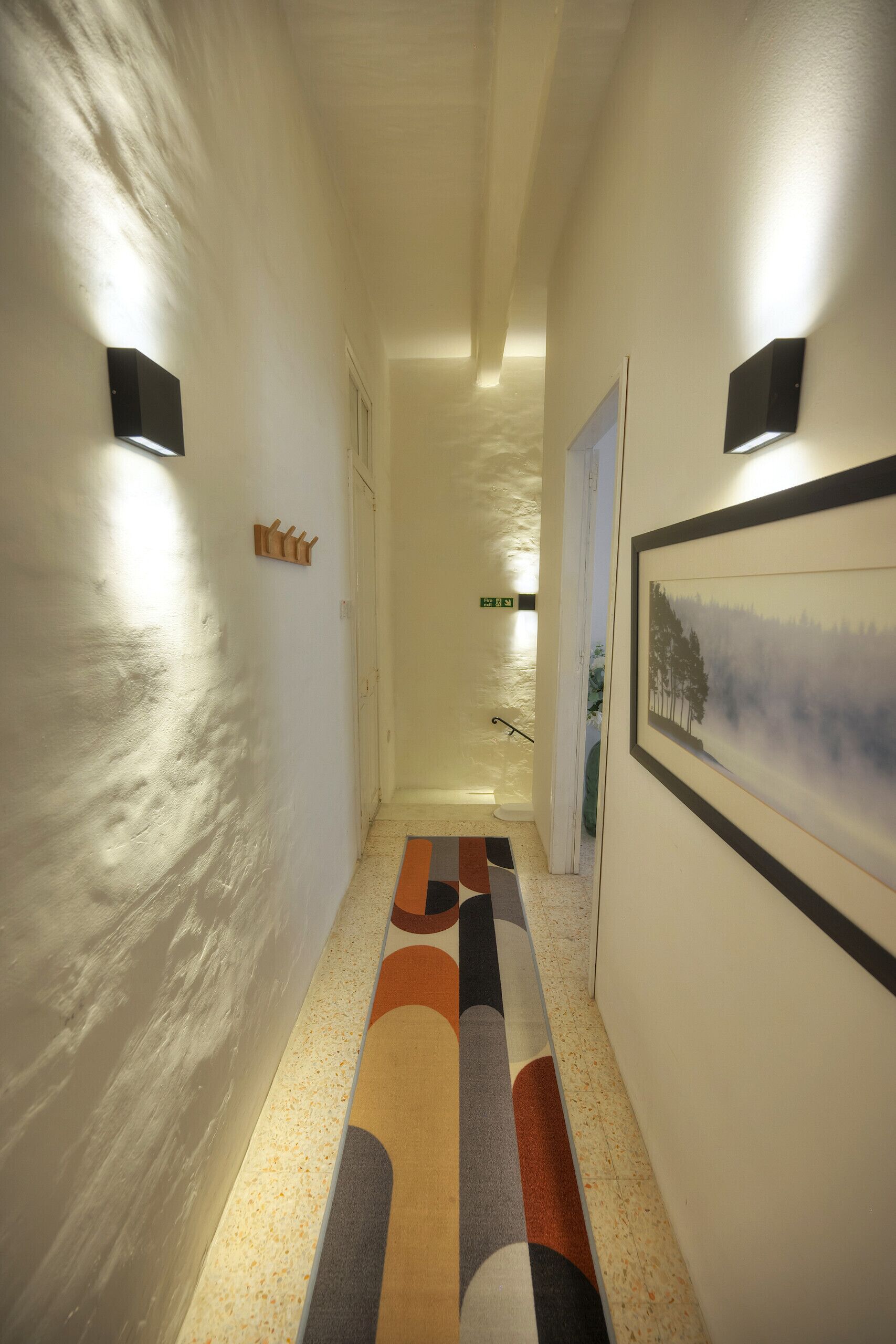 A hallway with a patterned carpet, a framed picture on the wall, and a door at the end.