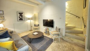 Una sala de estar moderna con sofá, mesa de centro y televisor. Se observa una escalera con pared amarilla y barandal negro.