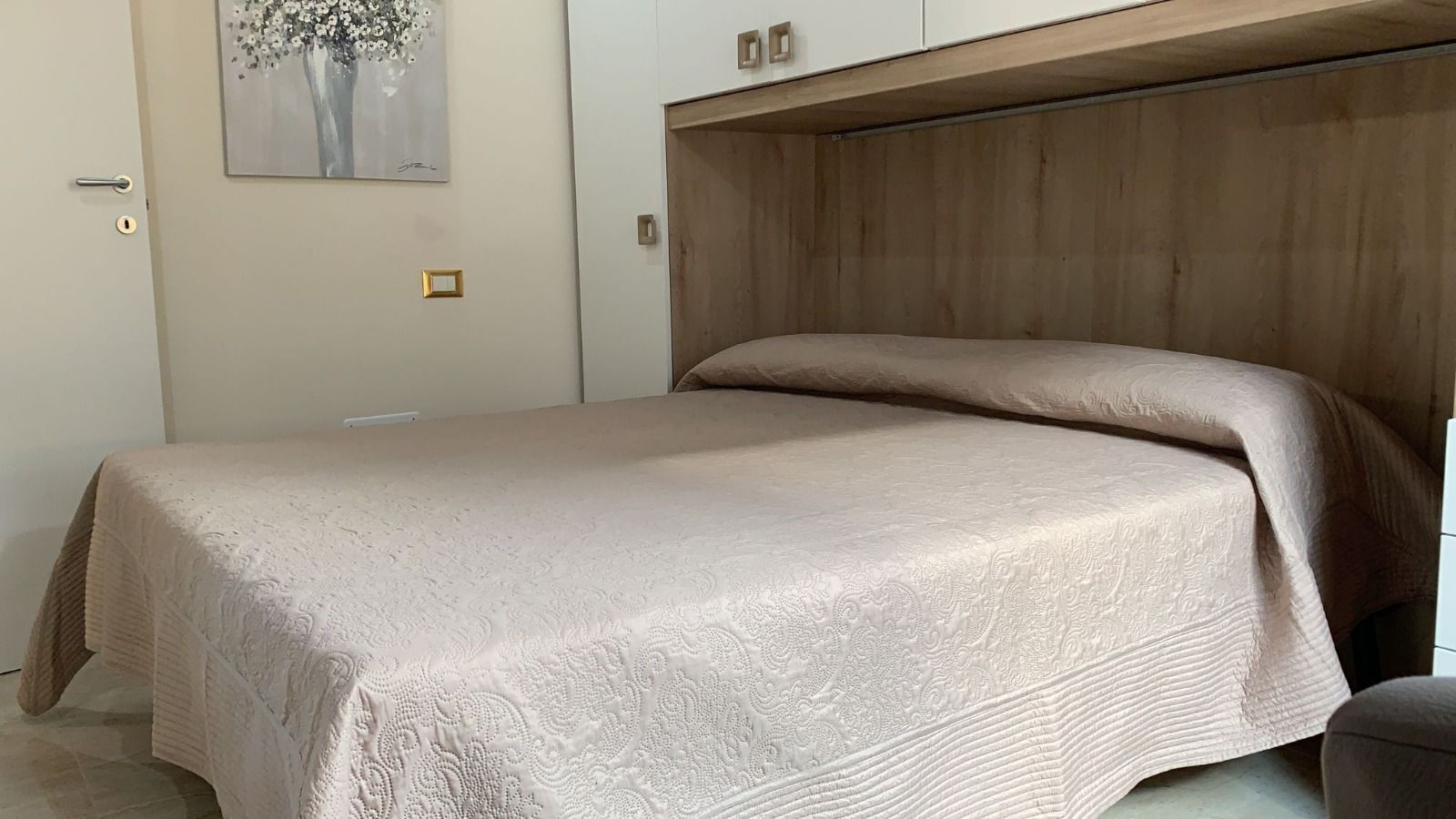 Een slaapkamer met een bed, een houten hoofdeinde, een deur en een lichtschakelaar op de muur.