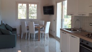 Eine moderne Küche mit weißen Schränken, einer Edelstahlspüle und einem eingebauten Backofen. Es gibt einen Essbereich mit Tisch und Stühlen, sowie einen an der Wand befestigten Fernseher.